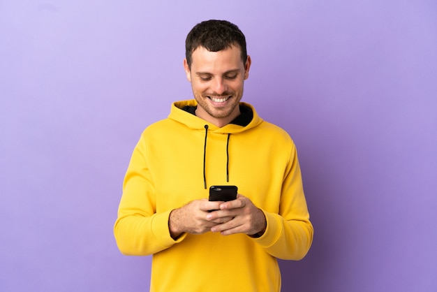 Brazilian man over isolated purple background sending a message with the mobile