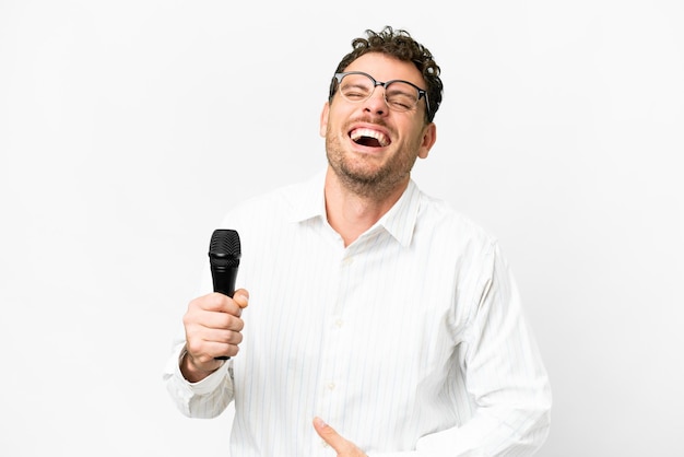 Photo brazilian man picking up a microphone over isolated white background smiling a lot