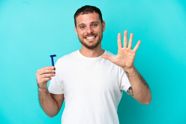 Brazilian man shaving his beard isolated on blue background counting five with fingers