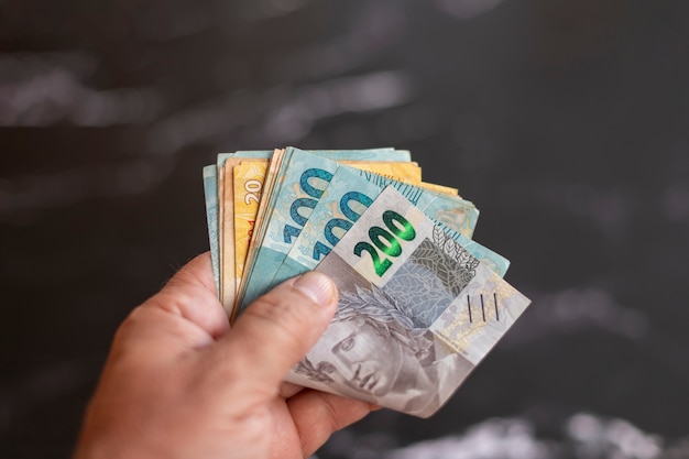 Brazilian money banknotes folded in hand, with dark background