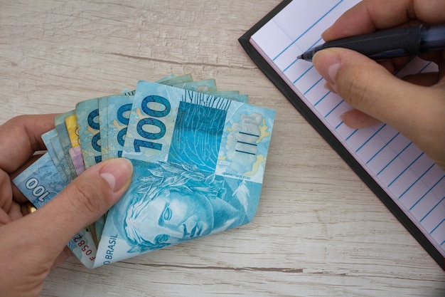 Brazilian money in paper hand making notes beside