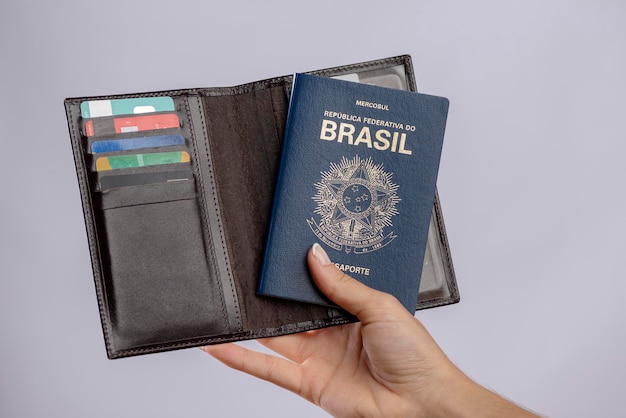 Brazilian passport in a hand with wallet credit cards and euro banknotes on a white background