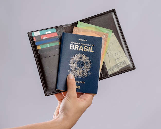 Brazilian passport in a hand with wallet credit cards and euro banknotes on a white background