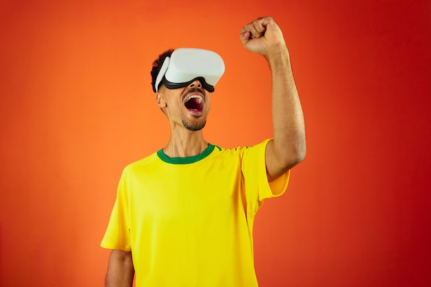 Brazilian Player Black Man Celebrating With VR Virtual Glasses Isolated on Orange background