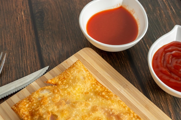 Brazilian snack pastel over wooden table with sauce pepper ketchup also fork and knife traditional pastry