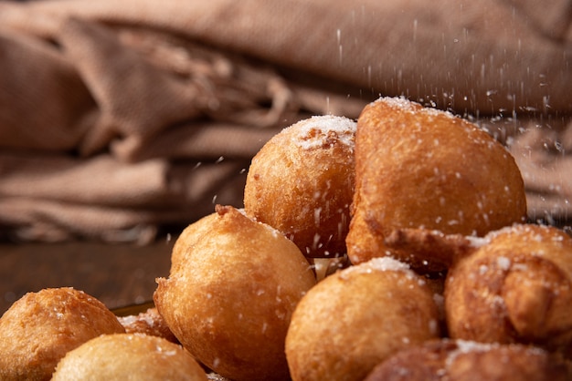 Brazilian sweet called bolinho de Chuva,  being sprinkled with sugar, rustic wood, selective focus.