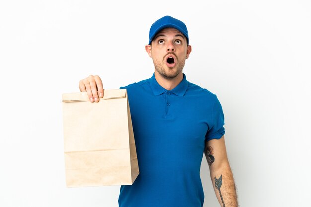 Brazilian taking a bag of takeaway food isolated on white background looking up and with surprised expression