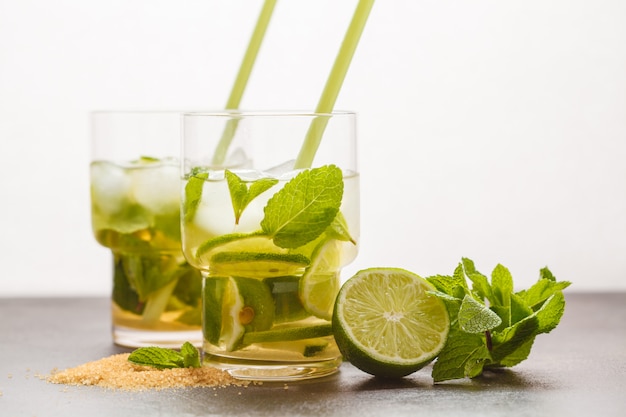 Brazilian traditional caipirinha with lime, sugar and mint in glasses. White background, dark table, copy space.