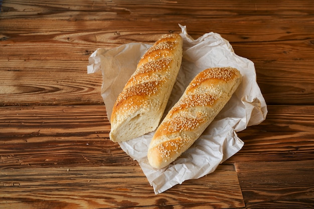 Bread baguette sprinkled sesame sesame with wrapping paper on wooden table