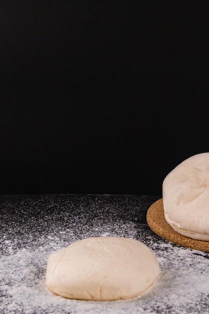 Bread concept a few bun doughs with flour being in the middle on the black background.