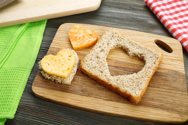 Bread slice with cut in shape of heart and cheese on table close up