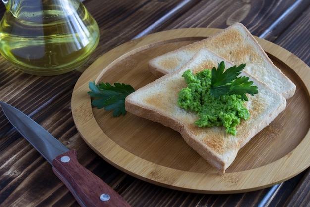 Bread toast with pea mash on the brown cutting board