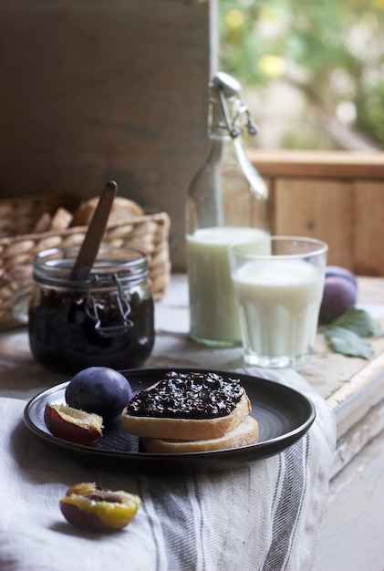 Bread toast with plum jam, served with milk and plums. Rustic style.