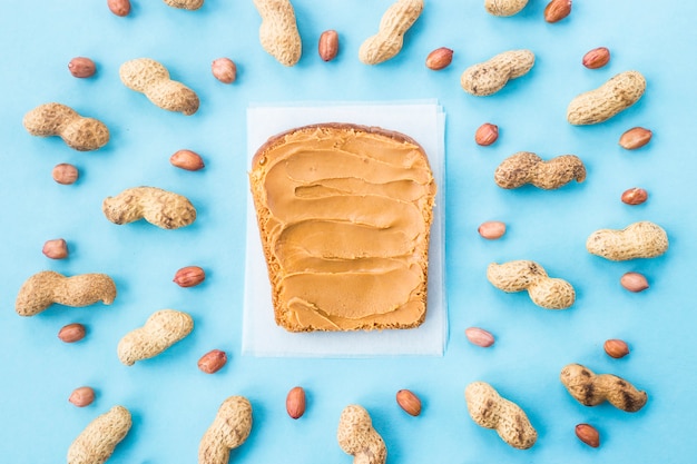 Photo bread toast with walnut paste among peanuts in shell and without on a blue background