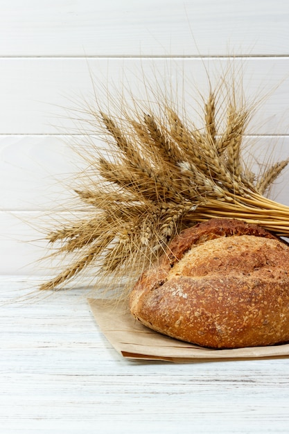 Bread and wheat on white wooden background