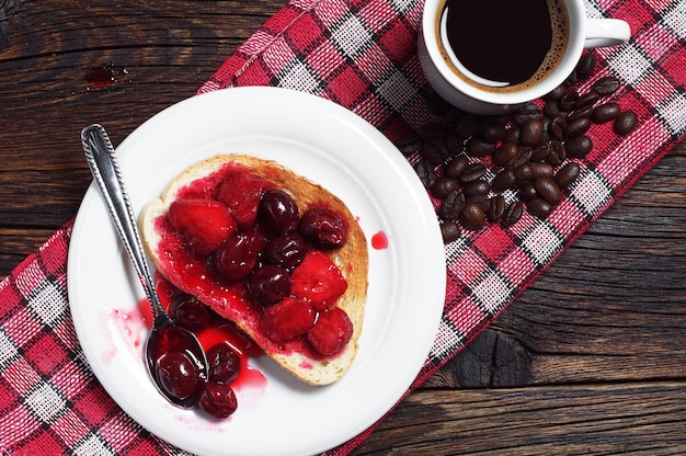 Bread with canned fruits and coffee
Toasted bread with canned cherries, strawberries and cup of coffee on rustic wooden table. Top view