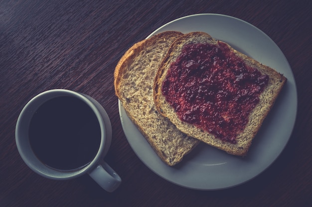 Bread with strawberry jam, and hot coffee on a wooden table. 