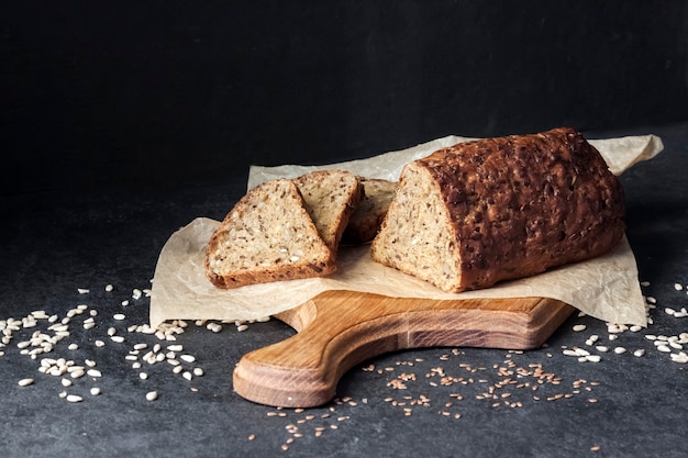 Bread with sunflower and flax seeds on a wooden cutting board on a black background