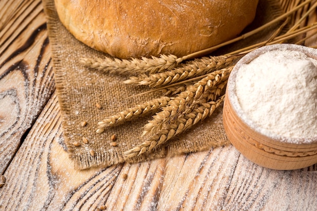 Bread with wheat flour spikes and grains on wooden table Agriculture and harvest concept