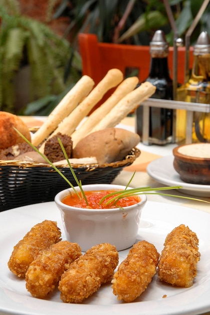 Breaded Manchego cheese fingers, with a basket of bread, olive oil and butter on a restaurant table