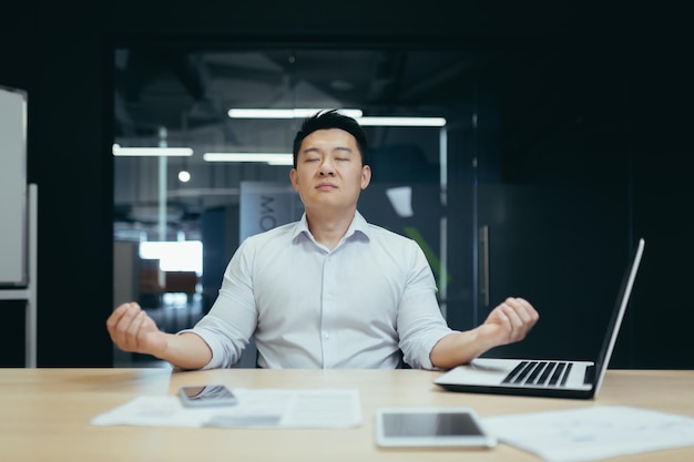 A break at work handsome young asian businessman man meditating at the workplace in the office