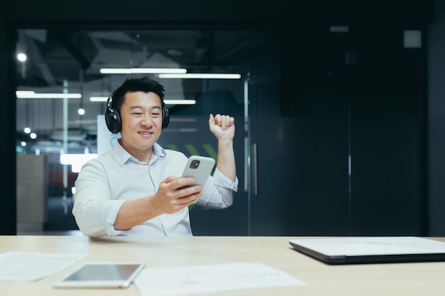 A break at work young handsome asian man freelancer listening to music on the phone in headphones