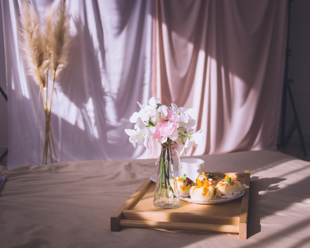 Breakfast in bed with coffee buns flowers on wooden tray in hotel bed or at home Window light