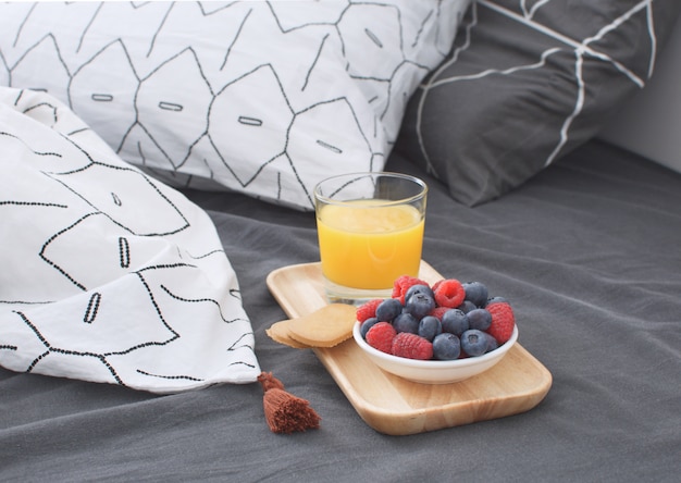 Breakfast bed Wooden tray Early morning  interior Geometric sheet and pillow case Berries Orange juice Biscuits