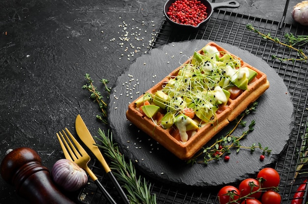 Breakfast Belgian waffles with avocado salted fish and microgreen On a black stone plate