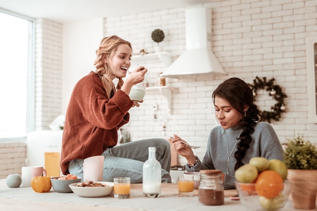 Breakfast bowl . Appealing positive girls carrying big spoons and eating cereals while wearing warm sweaters