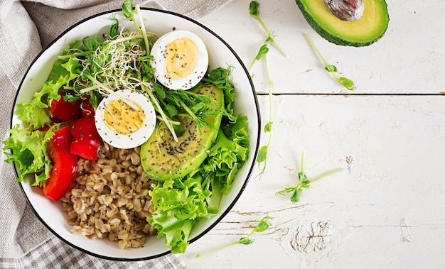 Breakfast bowl with oatmeal, paprika, avocado, lettuce, microgreens and boiled egg.