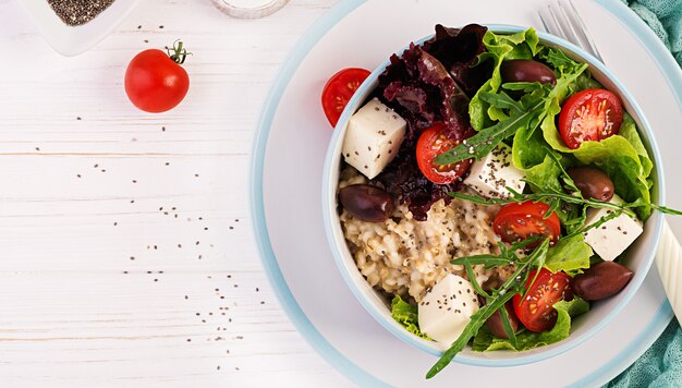 Breakfast bowl with oatmeal, tomatoes, cheese, lettuce, and olives