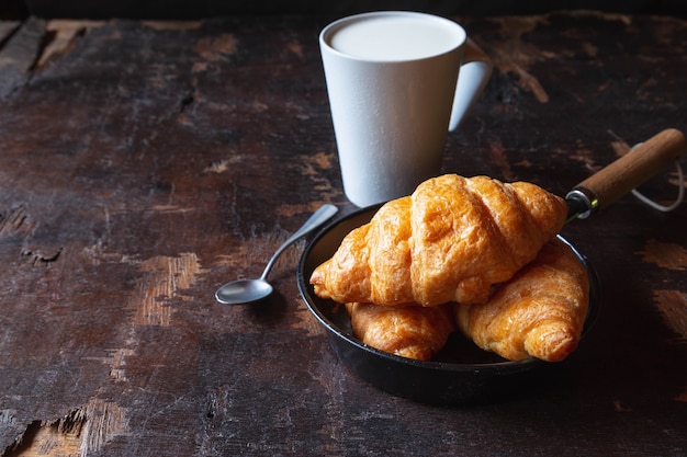 Breakfast bread, croissants and fresh milk on the wooden table.