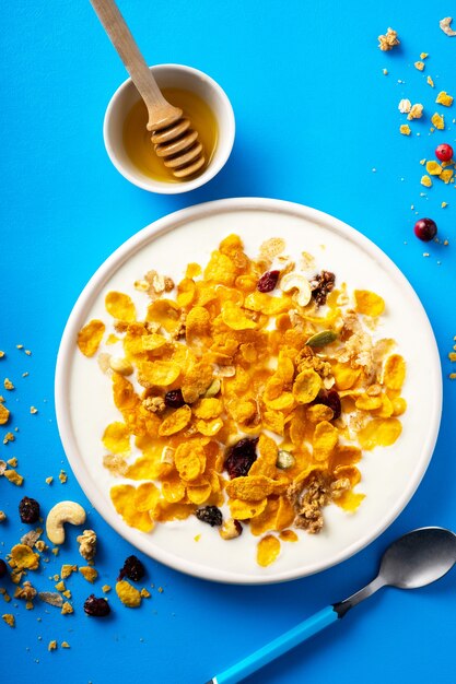 breakfast cereal cornflakes nuts seeds berries and honey in a bowl with milk on a blu bac