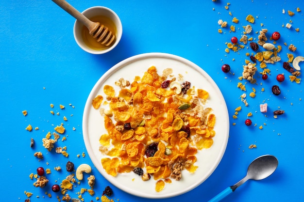 Breakfast cereal Cornflakes nuts seeds berries and honey in a bowl with milk