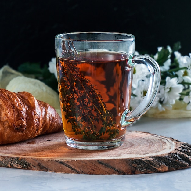 Breakfast cup of tea with thyme and croissant