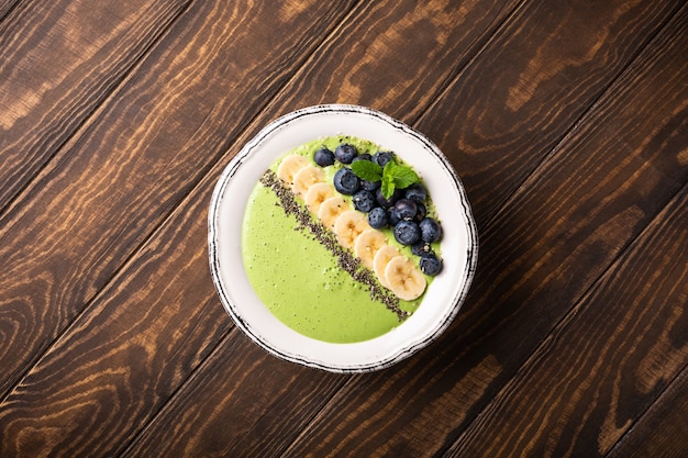 Breakfast detox green smoothie bowl from banana and spinach on wooden surface