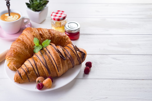 Breakfast freshly baked croissant decorated with jam and chocolate