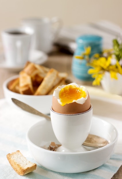 Breakfast from soft-boiled egg, bread toast, coffee with cream and fresh newspaper.