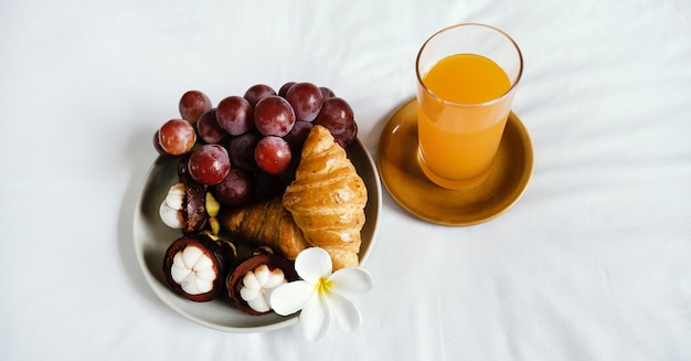 Breakfast, fruit, croissants, orange juice on a white bedsheet, Healthy food concept.