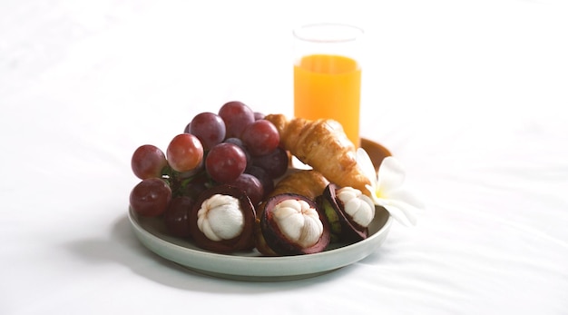 Breakfast, fruit, croissants, orange juice on a white bedsheet, Healthy food concept.