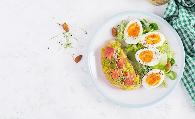 Breakfast. Healthy open sandwich on  toast with avocado and salmon, boiled eggs, herbs, chia seeds on white plate  with copy space. Healthy protein food. Top view, overhead