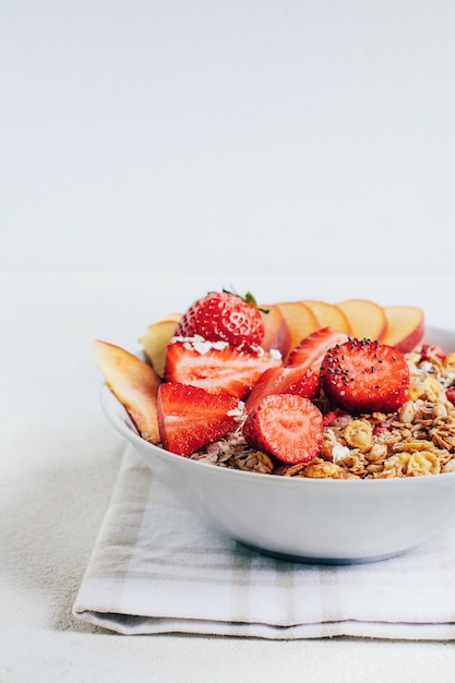 Breakfast oatmeal cereal granola with strawberries and peach in a white plate on a white plate