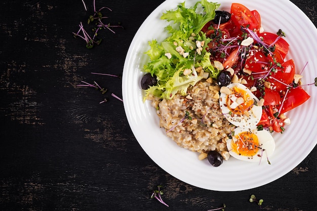 Breakfast oatmeal porridge with boiled egg cherry tomatoes olives nuts and microgreens Healthy balanced food Top view overhead