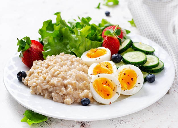 Breakfast oatmeal porridge with boiled eggs cucumber and strawberry Healthy balanced food