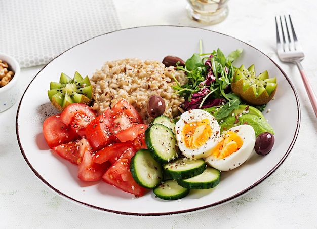 Breakfast oatmeal porridge with boiled eggs fresh salad and kiwi Healthy balanced food