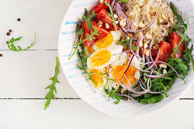 Breakfast oatmeal porridge with boiled eggs tomatoes and red onions Healthy balanced food Trendy food Top view flat lay