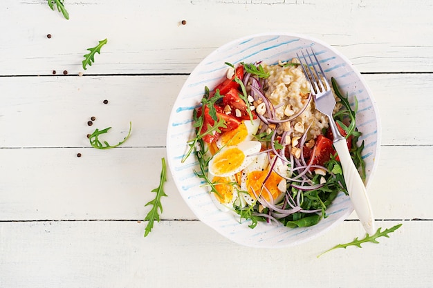 Breakfast oatmeal porridge with boiled eggs tomatoes and red onions Healthy balanced food Trendy food Top view flat lay