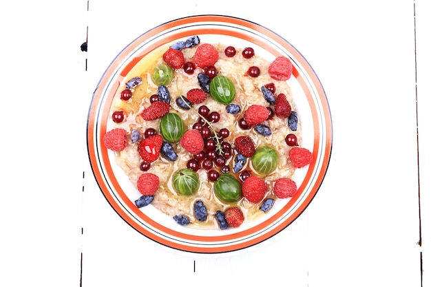 Breakfast oatmeal with berries and honey on white wooden background flat style top view overhead sum...