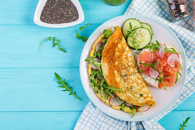 Breakfast. Omelette with radish, green arugula and sandwich with salmon on white plate